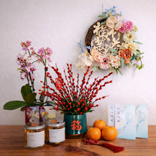 Decorative items including flowers, jars, and a wreath on a wooden surface with a white wall background.